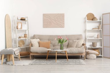 Oturma odasının içinde kanepe, raflar, güzel lale çiçekleri ve sehpanın üzerinde dergiler var.