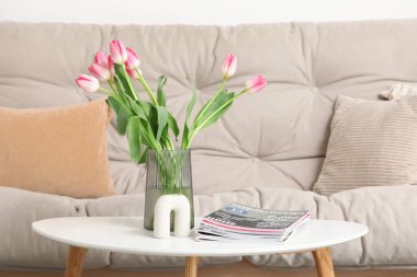 Oturma odasındaki kanepenin yanındaki sehpanın üzerinde dergiler olan güzel lale çiçekleri vazosu.