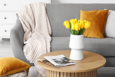 Oturma odasındaki kanepenin yanındaki sehpanın üzerinde dergiler olan güzel lale çiçekleri vazosu.