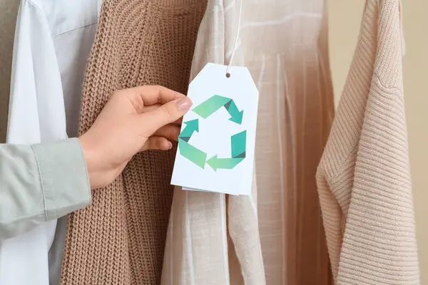 Giysilerdeki geri dönüşüm etiketini bej arka planda tutan kadın