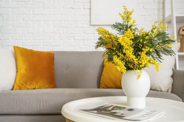 Vase with mimosa flowers and magazine on table in living room