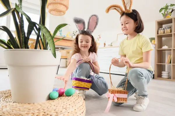 Mutfakta Paskalya yumurtası arayan tavşan kulaklı ve sepetli şirin küçük kızlar.