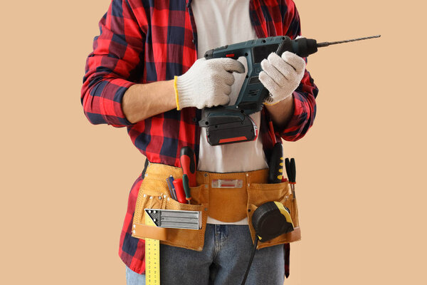 Мужчина строитель в строительных перчатках с дрелью и профессиональными инструментами на бежевом фоне, крупным планом