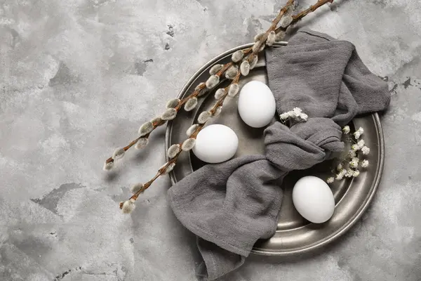 Paskalya yumurtaları, söğüt dalları, çiçekler ve gri grunge arka planda peçeteyle şenlik masası.