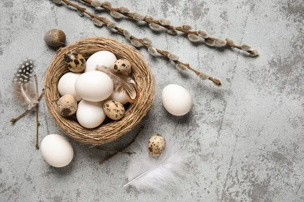 Paskalya yumurtaları, tüyleri ve gri grunge arka planında söğüt dalları olan yuva.