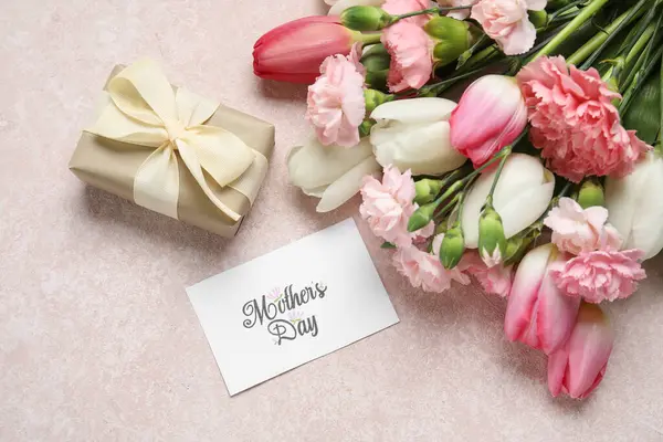 Bir buket farklı güzel çiçek, tebrik kartı ve bej arka planda hediye kutusu. Anneler Günü kutlaması