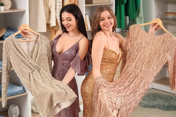 Şık genç kadınlar butikte parlak elbiseler seçiyor.
