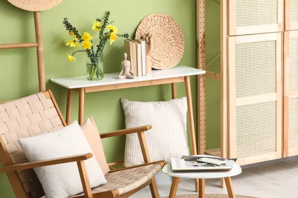 Oturma odasındaki yeşil duvarın yanında dergileri ve kitapları olan güzel nergis çiçekleri vazosu.