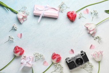 Güzel lalelerden yapılmış çerçeve, çingene çiçekleri, kağıt kalpler, hediye kutuları ve açık mavi arka planda fotoğraf makinesi. Anneler Günü kutlaması