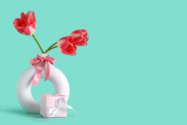 İçinde güzel lale çiçekleri ve turkuaz arka planda hediye kutusu olan vazo. Anneler Günü kutlaması