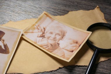 Ahşap arka planda büyüteci olan akrabaların eski fotoğrafları, yakın plan. Aile ağacı kavramı