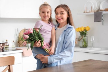 Anneler Günü için annesini mutfakta lalelerle selamlayan tatlı küçük bir kız.