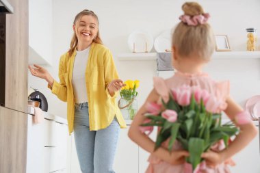 Küçük bir kız mutfakta annesine bir buket lale tutuyor, yakın plan. Anneler Günün kutlu olsun.