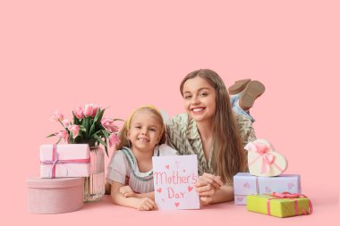 Anneler Günü 'nde annesini hediyeler, laleler ve kartpostallarla karşılayan tatlı küçük kız pembe arka planda yatıyor.