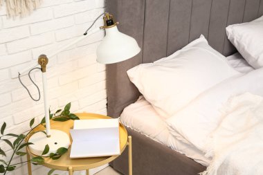 Lamba ve kitap, aydınlık odada yatağın yanındaki masada.