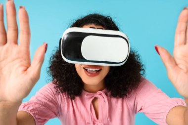 Mavi arka planda VR gözlüklü genç Afro-Amerikalı kadın.