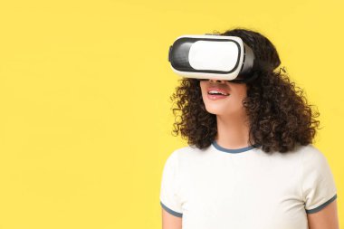 Sarı arka planda VR gözlüklü genç Afro-Amerikalı kadın.