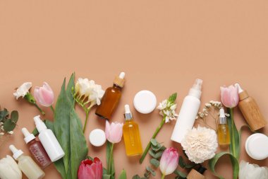 Farklı kozmetik ürünleri ve kahverengi arka planda güzel çiçekler.