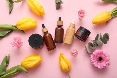 Farklı kozmetik ürünleri ve pembe arka planda güzel çiçekler.