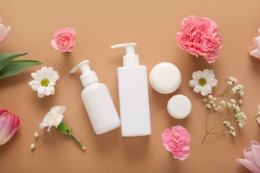Farklı kozmetik ürünleri ve kahverengi arka planda güzel çiçekler.