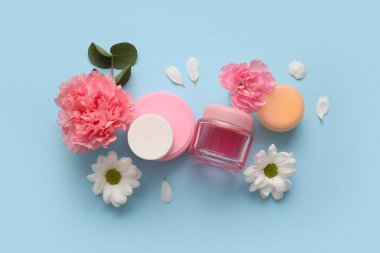 Farklı kozmetik ürünleri ve mavi arka planda güzel çiçekler.
