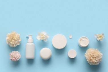 Farklı kozmetik ürünleri ve mavi arka planda güzel çiçekler.