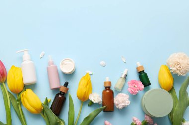 Farklı kozmetik ürünleri ve mavi arka planda güzel çiçekler.