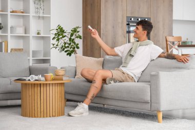 Kanepedeki genç adam evdeki klimayı açıyor.