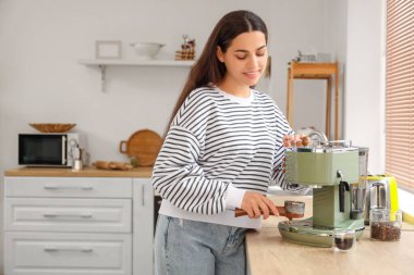 Mutfakta modern kahve makinesi olan güzel, genç ve mutlu bir kadın.