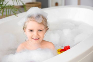 Şirin küçük kız banyo yaparken köpük ve oyuncaklarla banyo yapıyor.