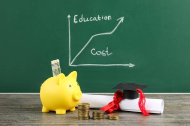 Kumbarada para, diploma ve mezuniyet şapkası yeşil tahtanın yanında. Öğrenci kredisi kavramı