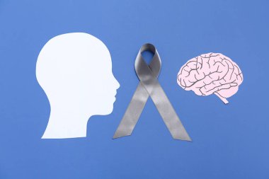 Beyni ve mavi arka planda gri farkındalık kurdelesi olan kağıt insan kafası. Kanser kavramı