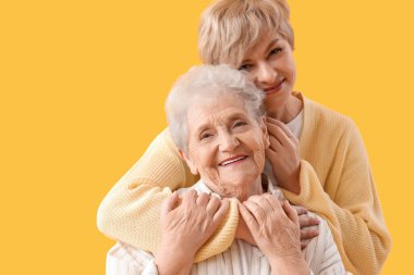 Yetişkin bir kadın sarı arka planda annesine sarılıyor.