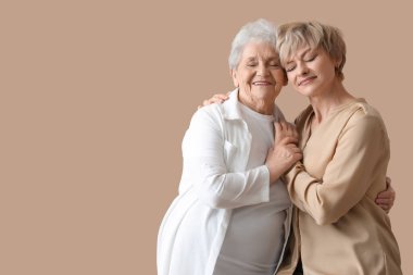 Bej arka planda annesi kucaklayan olgun bir kadın.