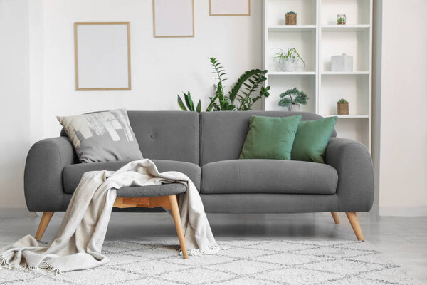 Comfortable sofa with cushions and plaid, shelving unit and frame on wall in living room