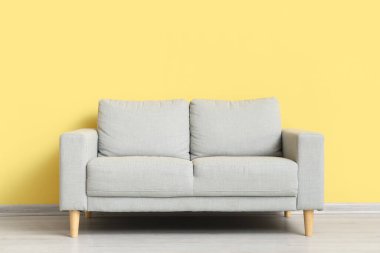 Stylish grey sofa near yellow wall