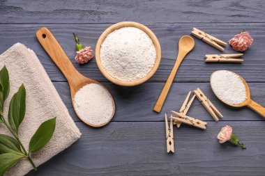 Çamaşır deterjanları, mandallar, karanfil çiçekleri ve gri ahşap arka planda bitki dalları.