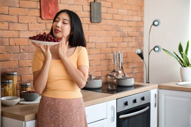 Mutfakta bir kase olgun kirazlı güzel Asyalı kadın.