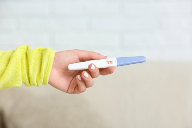 Bulanık arka planda pozitif hamilelik testi olan kadın eli, yakın plan.