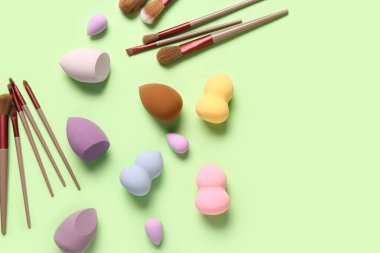 Yeşil arkaplanda makyaj süngerleri ve fırçalar