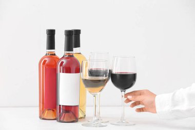 Aydınlık arka planda farklı şaraplardan yapılmış kadehlerle bir kadın eli.