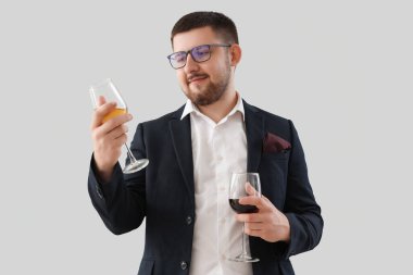 Genç şarap garsonunun elinde gri arka planda farklı türde şarap bardakları var.