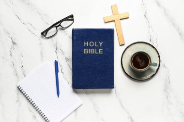 Kutsal İncil, haç, defter, beyaz mermer arka planda bir fincan kahve ve gözlük.