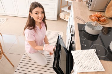 Young woman opening electric oven in kitchen