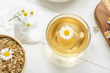 Beyaz ahşap arka planda kurutulmuş papatya çayı ve kase.