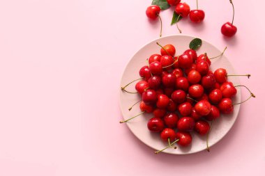 Pembe arka planda bir tabak tatlı kiraz.