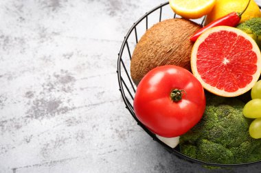 Gri arka planda farklı taze meyve ve sebzelerin olduğu sepet, yakın plan.