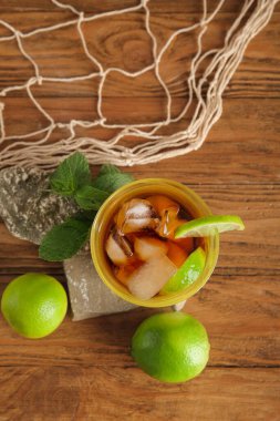 Bir bardak soğuk Küba Libre kokteyli ve ahşap arka planda ağ olan taşlar.