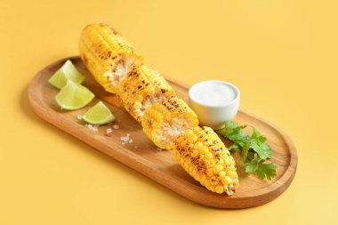 Tahta tahta tahta, lezzetli ızgara mısır koçanı ve sarı arka planda sos.