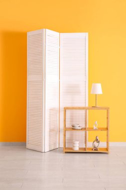 Turuncu duvarın yanında katlanan ekran ve raf ünitesi